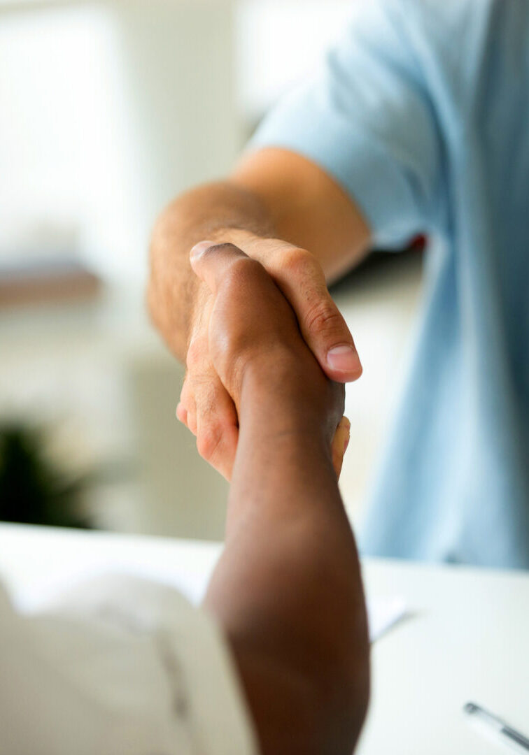 Close up of multiracial handshake at office desk. Caucasian worker shaking hand of black colleague, welcoming at new workplace, greeting, being promoted. Cooperation, support, making agreement concept